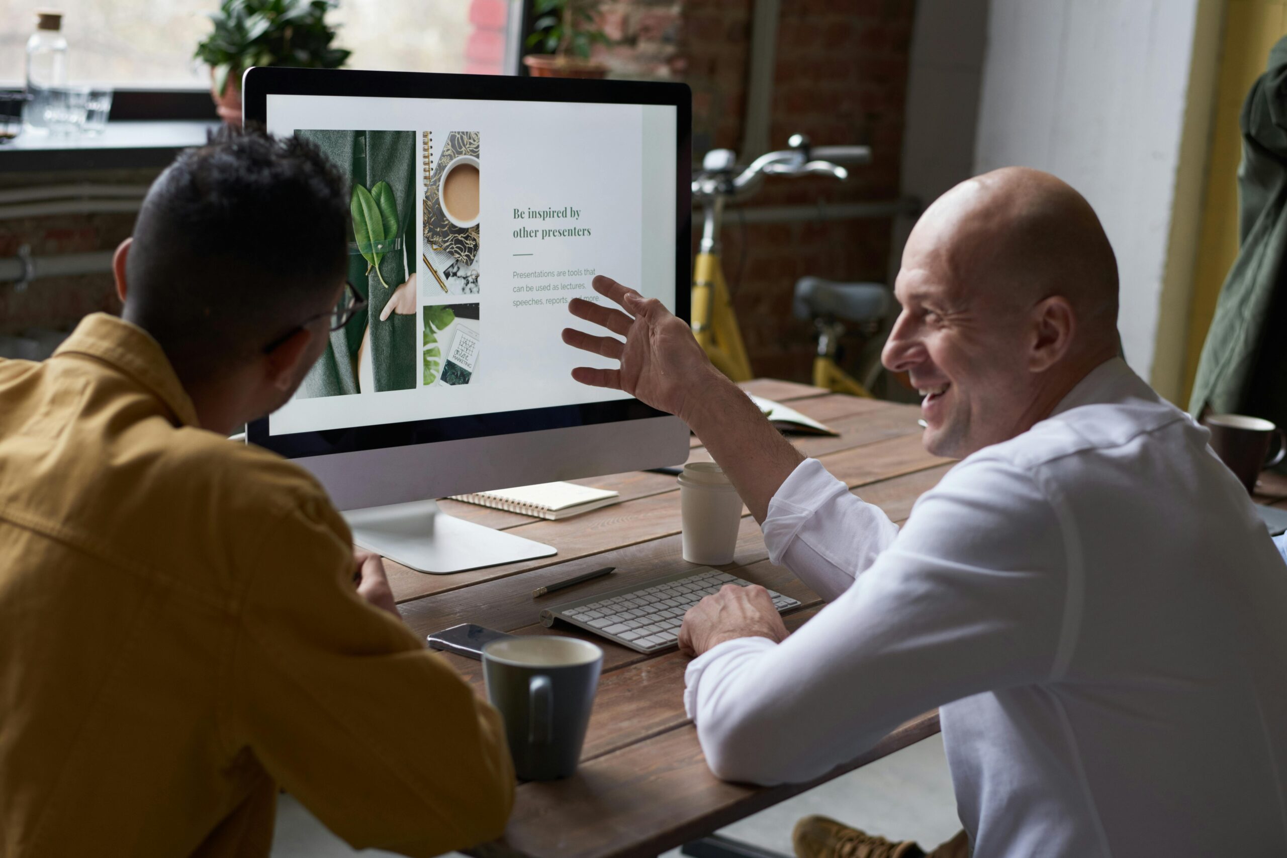 Picture of 2 men discussing a website they are building while sitting at a desk in front of a computer.